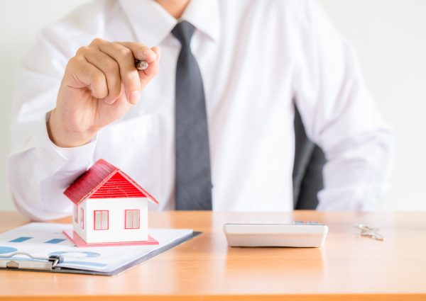 Home salesman stretches holding black pen, model house on wooden desk, Model house with red roof.